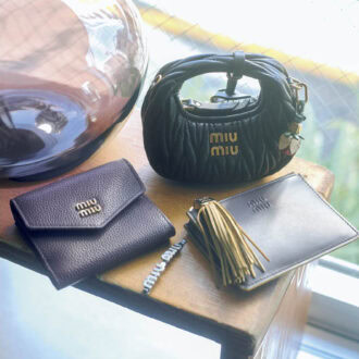 上から、細部まで精巧に再現された完成度の高さ。花のチャームまで揃っていてワクワク。バッグチャーム［H9・5×W12×D5］￥161,700、バッグチャームにつけたチャーム￥31,900、ボリューミーなフリンジとロゴ入りのメタルパーツがインパクト大。後ろにカードスロット、取り外し可能なキーリング付き。カードホルダー［H8×W11、カード入れ3］￥83,600、メタルのロゴをのせたフロントフラップと、きれいなシボのボルドーカラーがクラシカルで上品。ウォレット［H8×W9×D2、カード入れ3］￥88，000、アイコニックなロゴデザイン。ヘアピン￥52,800※すべて予定価格（ミュウミュウ／ミュウミュウ クライアントサービス）