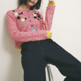 立体的なフラワーモチーフがついたピンクのカーディガンとデニムパンツを着た女性