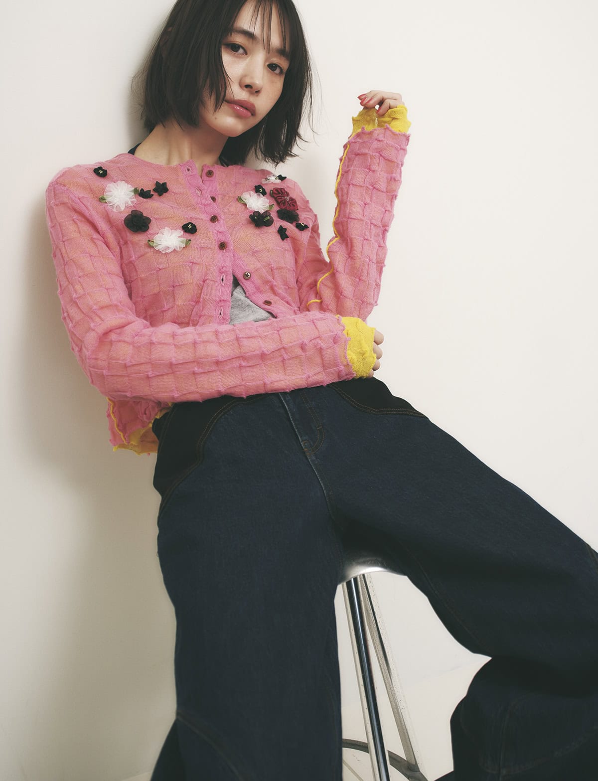 立体的なフラワーモチーフがついたピンクのカーディガンとデニムパンツを着た女性